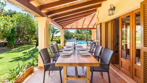 Une terrasse extérieure avec une table en bois dressée pour le repas, entourée de chaises, et une piscine en arrière-plan.