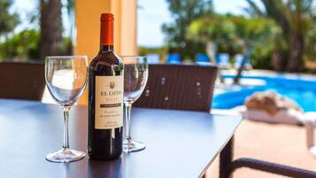 A bottle of El Coto de Rioja wine and two glasses on a table with a pool view.