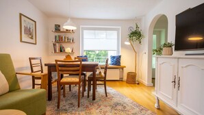 Un espace repas comprenant une table, des chaises, un tapis, une bibliothèque, un téléviseur et une plante.