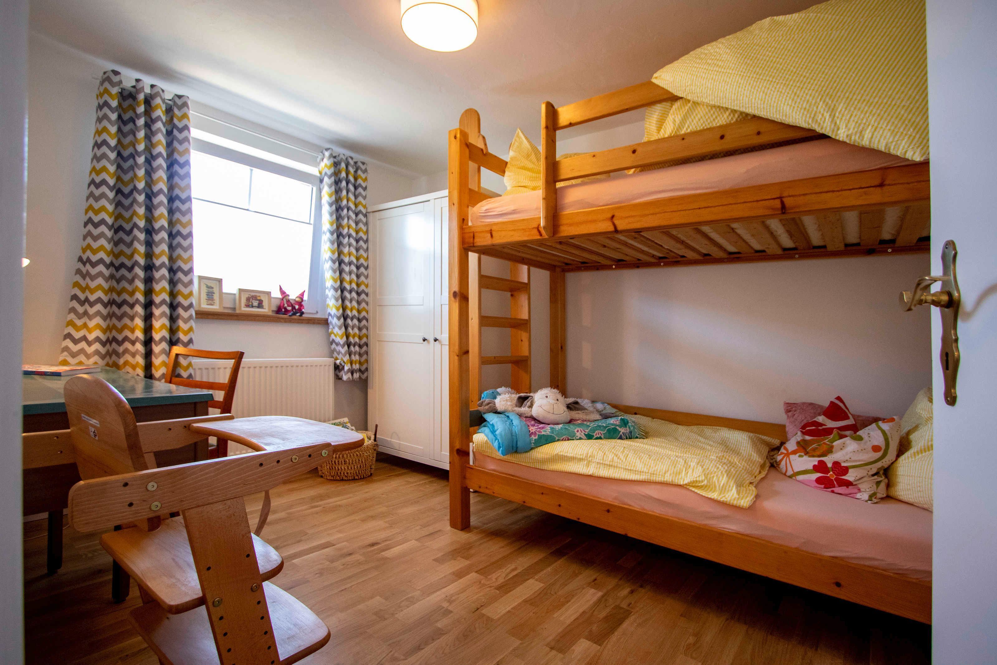 Un lit superposé avec une échelle en bois, un bureau avec une chaise et une fenêtre avec des rideaux.