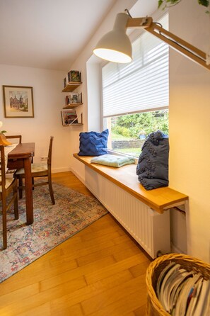 A cozy room with a wooden table, a bench with cushions, a radiator, a window with blinds, and a bookshelf with books. - Bauland Vacation Apartment - Paula's Vacation Home   (Buchen)