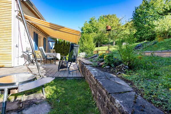 A wooden deck with outdoor furniture, a stone retaining wall, and a garden with various plants and a wooden fence.