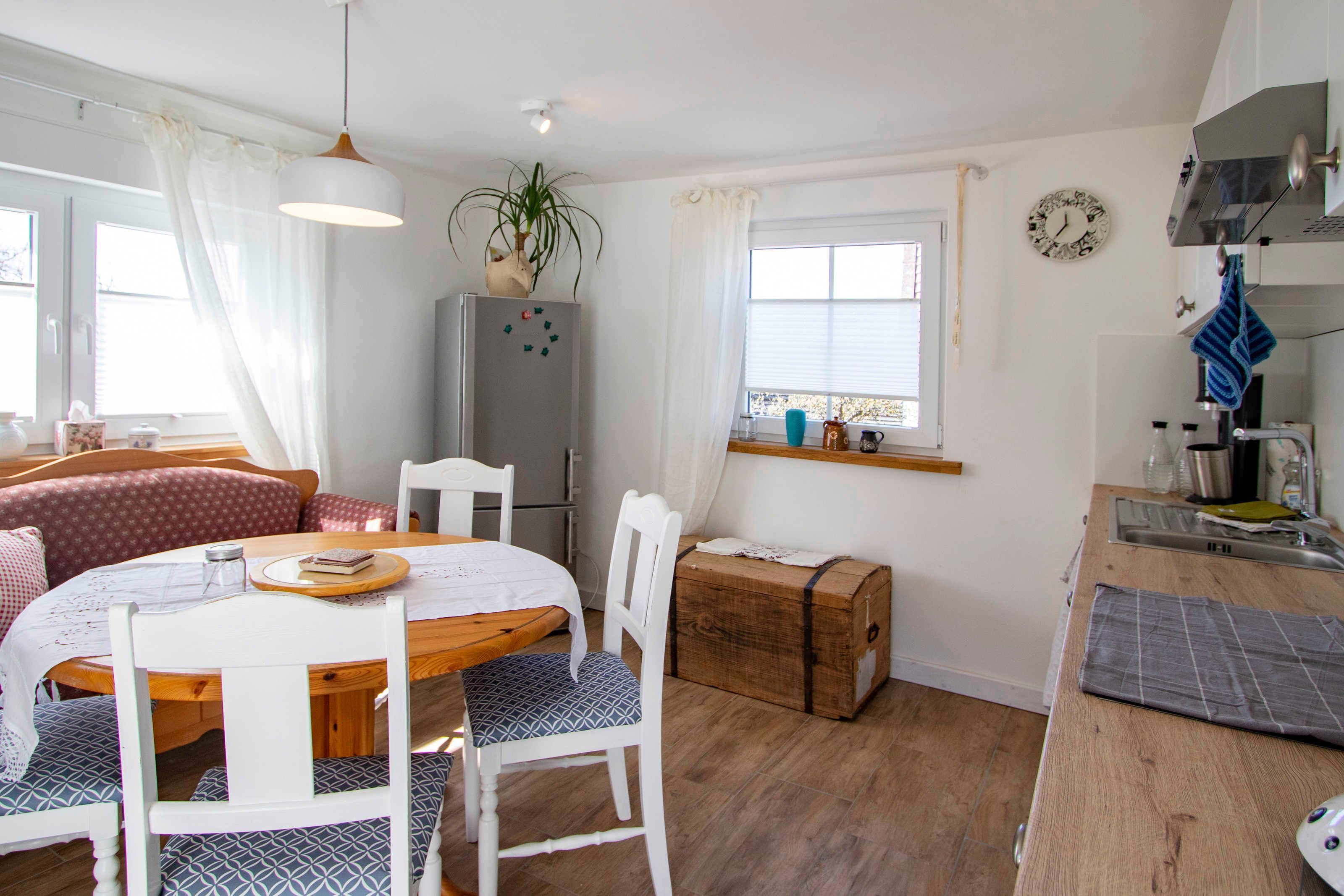 A compact kitchen with a dining area, wooden cabinets, and a window with curtains.