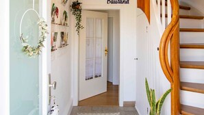 Un couloir avec un escalier en bois, un radiateur, un tapis à motifs en chevrons et une porte portant l’inscription « Bauland ».