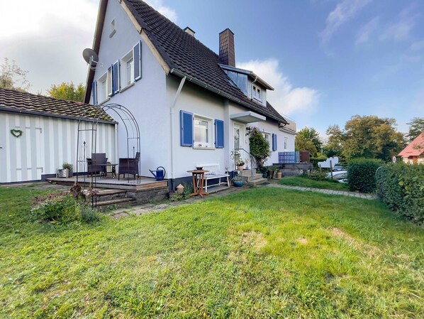 A two-story house with a covered patio, a small garden, and a car parked outside.