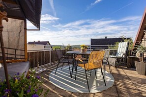 Eine Dachterrasse mit Tisch und Stühlen, ein Korbstuhl, ein kleiner Tisch mit einem Korb und Blick auf die Stadtlandschaft.