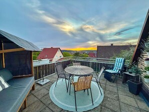 A rooftop terrace with a round table and chairs, a sofa, and potted plants. - Ferienwohnung Odenwald - Paulas Ferienhaus (Buchen)