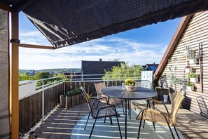 Une terrasse sur le toit avec une table ronde et des chaises, une clôture en bois et des plantes en pot.