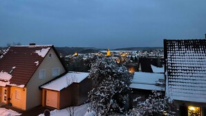 Un quartier résidentiel avec des maisons, un arbre recouvert de neige et des lumières scintillantes au loin.