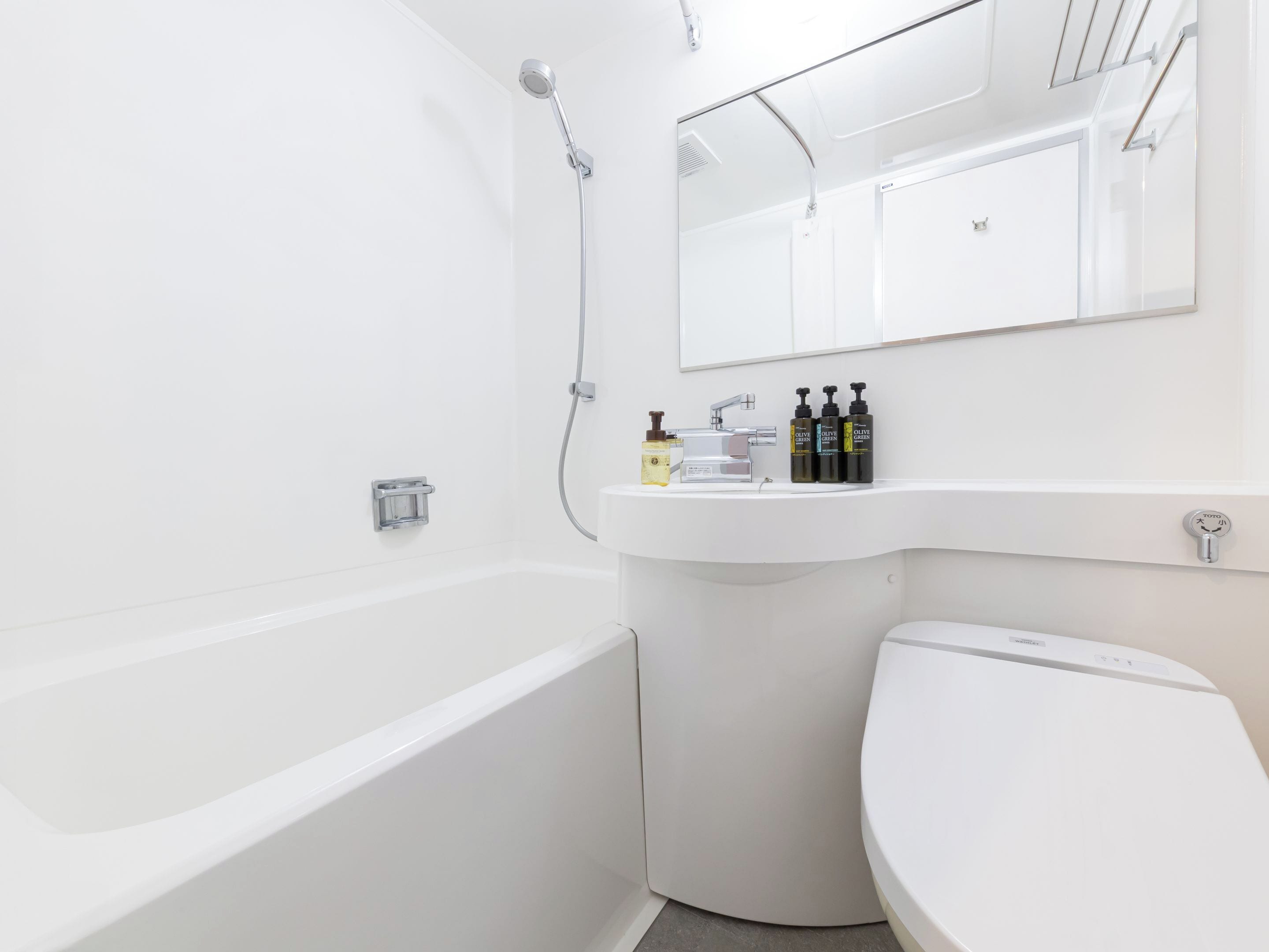 A modern bathroom with a white bathtub, a sink, and a toilet. There are toiletries on the sink counter.