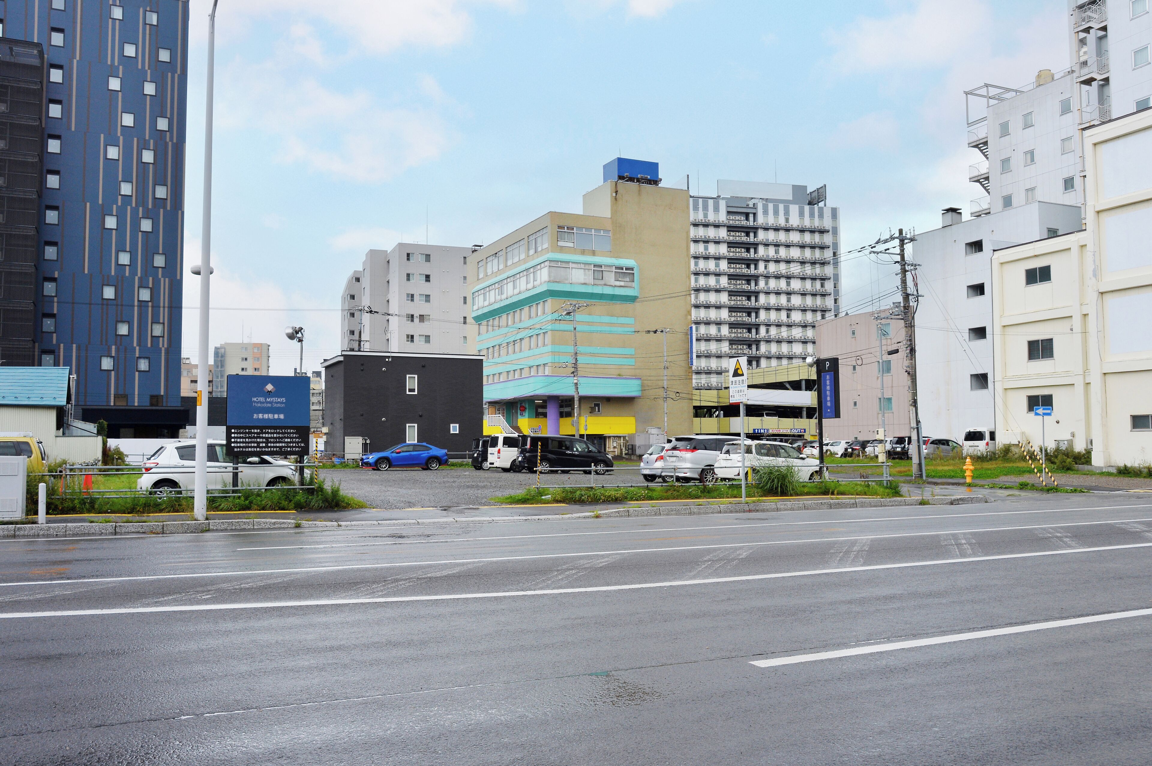A multi-story building with a blue and yellow facade, located at a city intersection with parked cars and a pedestrian crossing.
