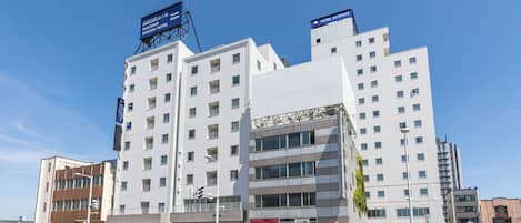 Un hotel de varios pisos con un diseño arquitectónico moderno, que destaca por una entrada imponente y señalización de servicios para huéspedes.