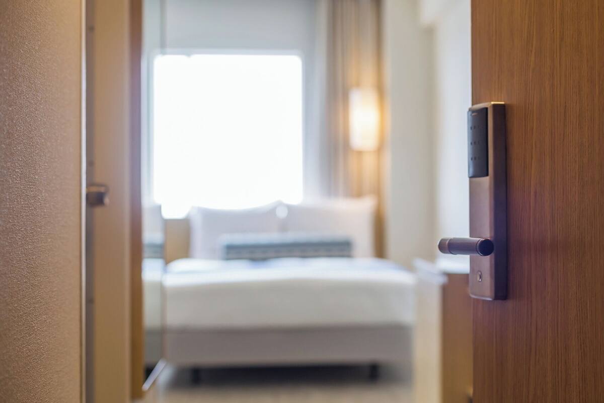 A hotel room with a bed, a bedside table, and a door with a lock.