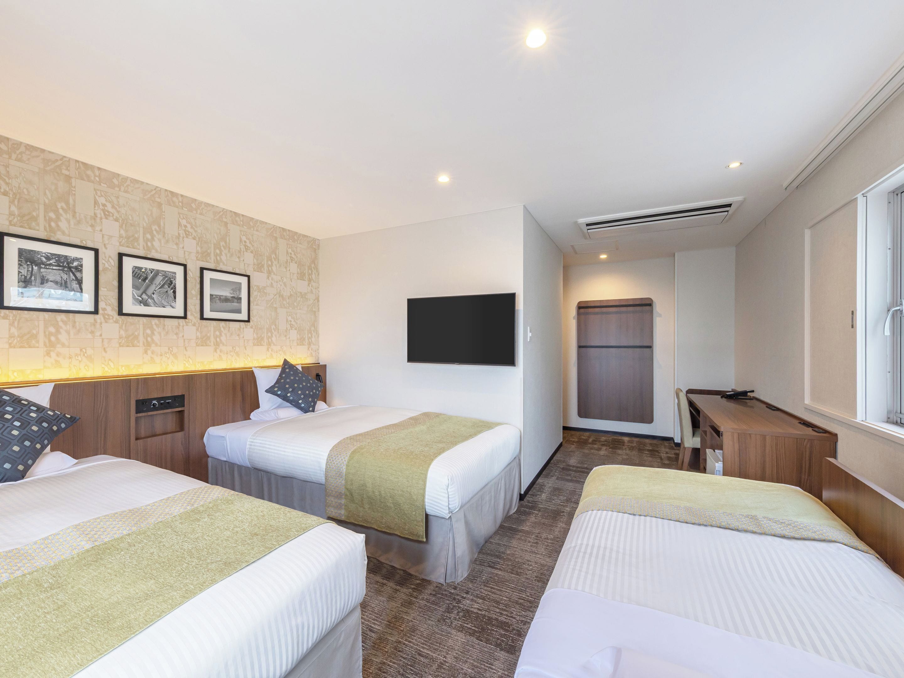 A hotel room with three beds, a flat-screen TV, a desk, and a wardrobe.