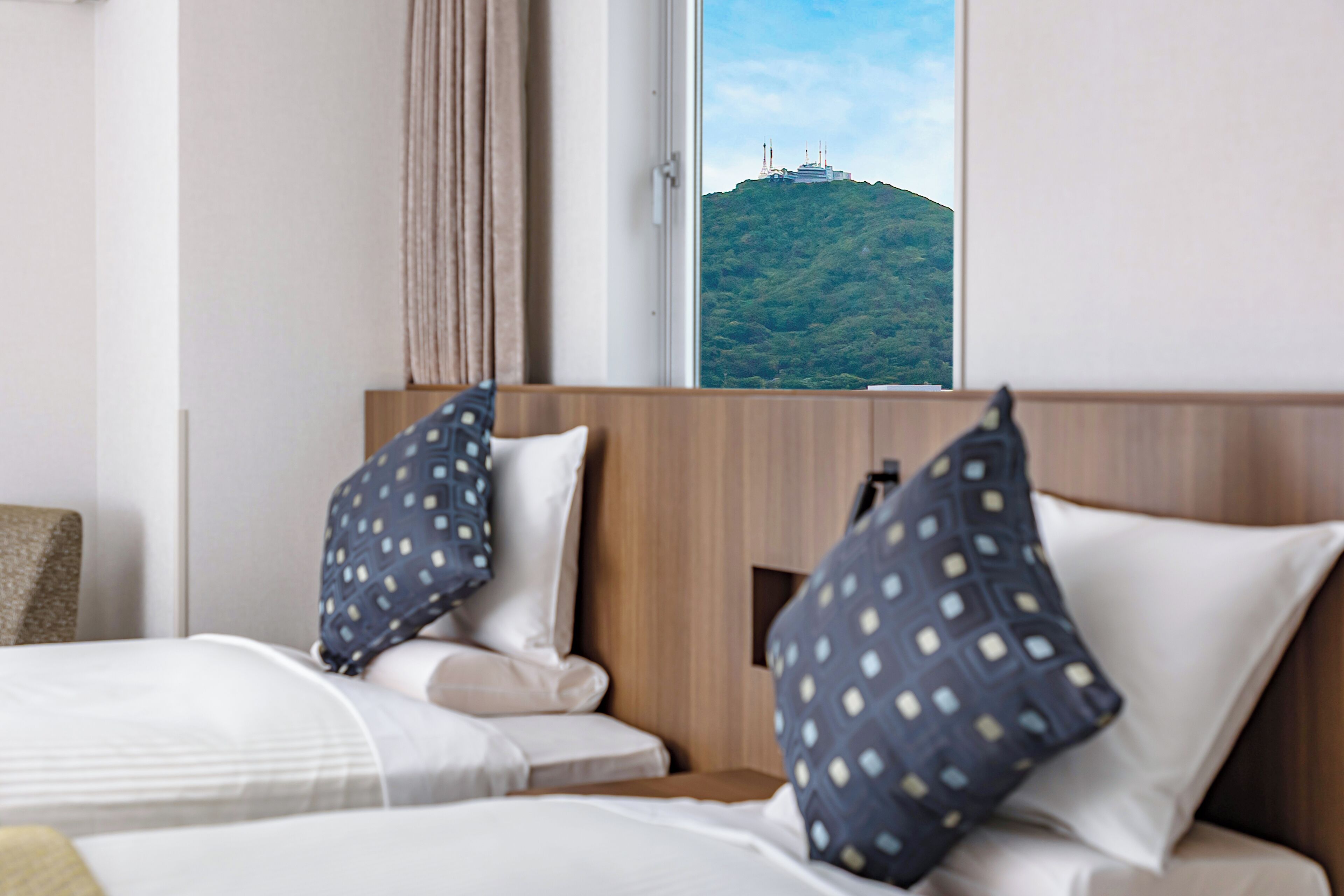 A hotel room with a bed, pillows, a window, and a view of a hill with structures.
