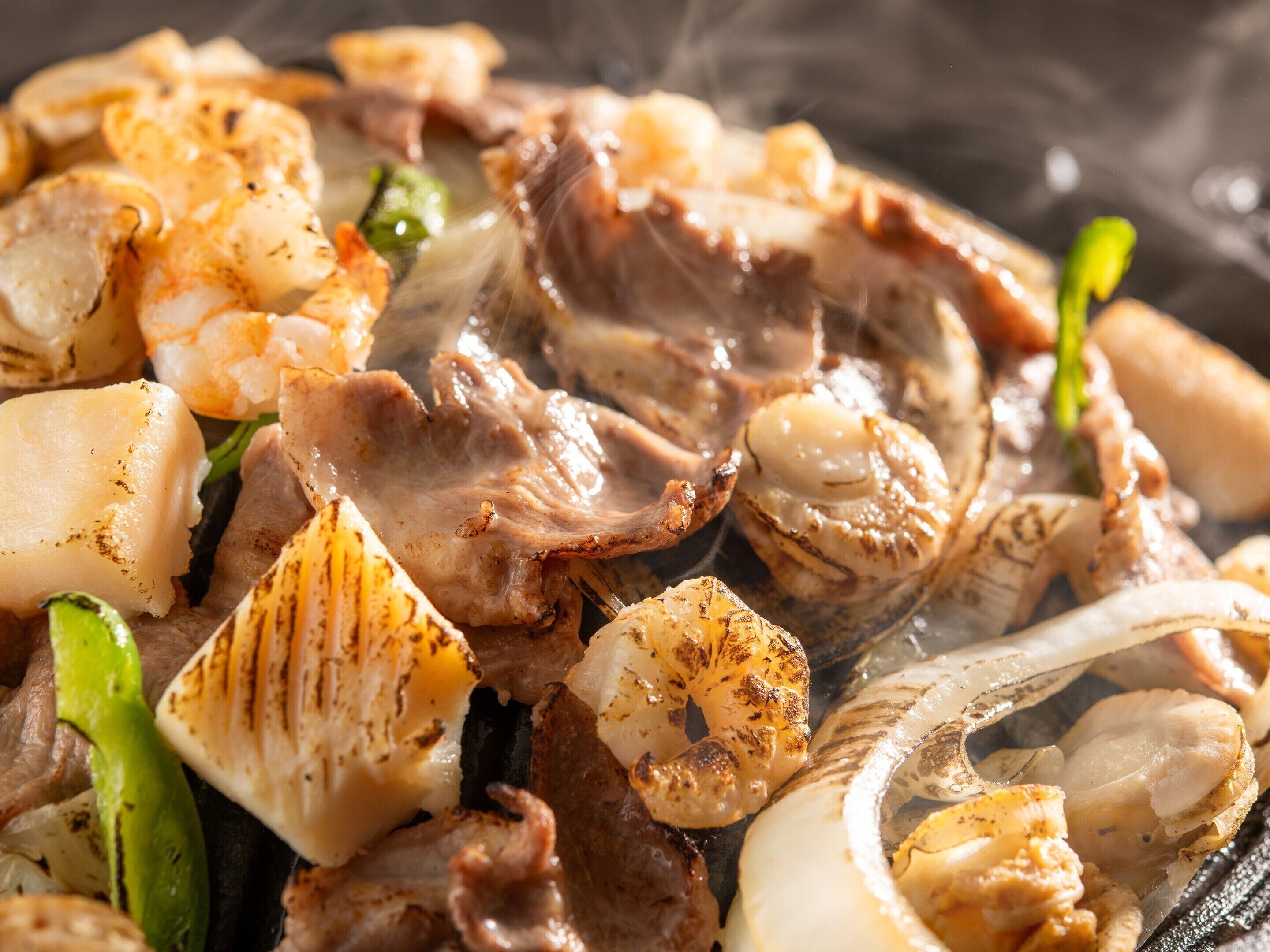 A close-up of grilled seafood, including shrimp and scallops, with visible char marks.