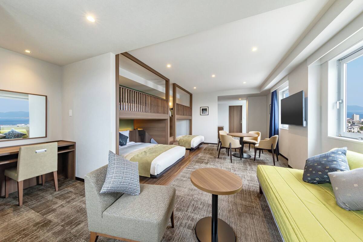 A hotel room with a bed, a desk, a chair, a sofa, a TV, and a window with a view.