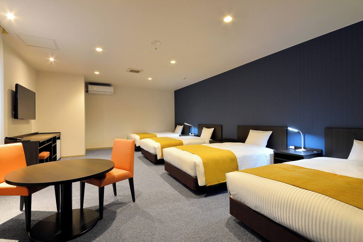 A hotel room with three beds, a desk, and a chair.