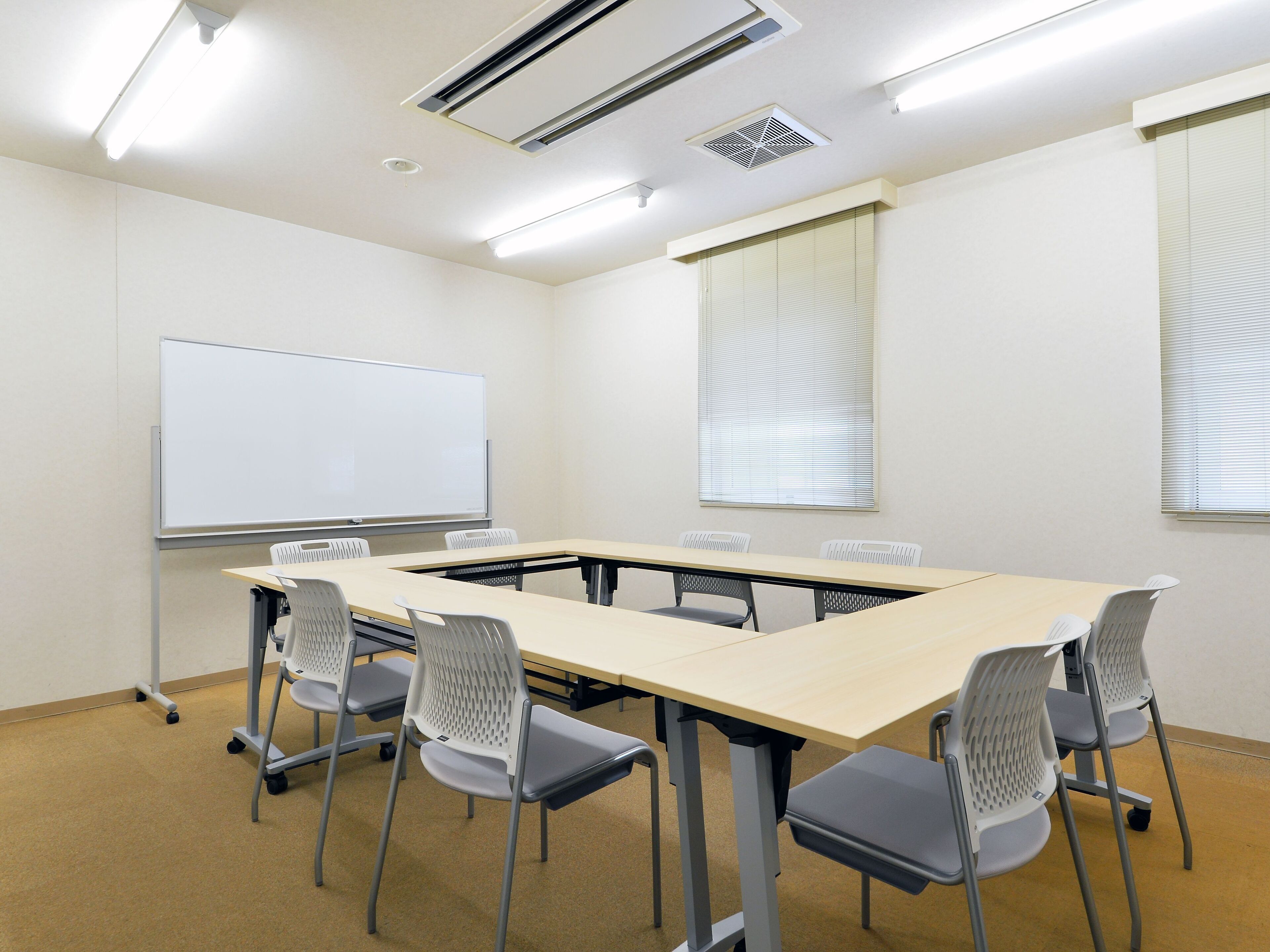 A conference room with a long table, six chairs, a whiteboard, and ceiling lights.