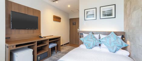 Una habitación de hotel moderna con televisor de pantalla plana, un escritorio de madera con mini refrigerador, una cama con almohadas estampadas y aire acondicionado de pared.