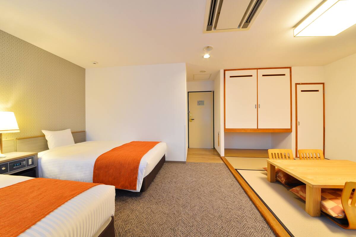 A hotel room with two beds, a desk, a chair, a table, and a wardrobe.