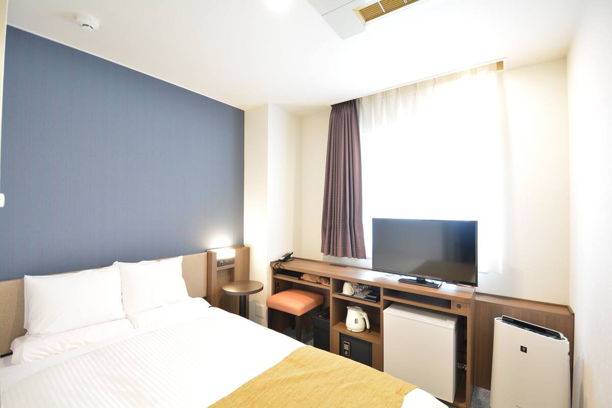 A hotel room with a bed, a desk with a computer, a television, and a small refrigerator.
