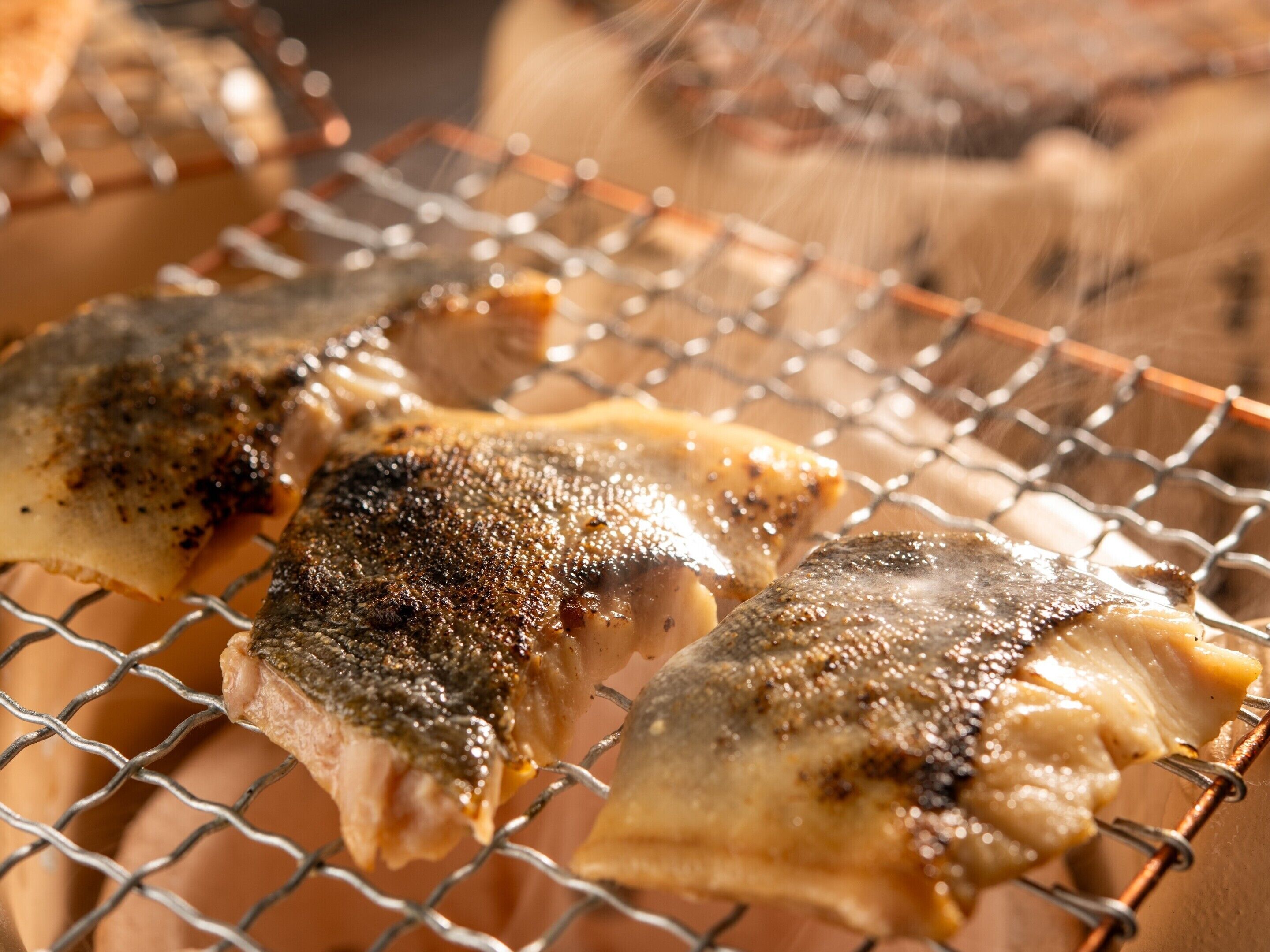 Tres piezas de pescado sobre una rejilla, probablemente a la parrilla.