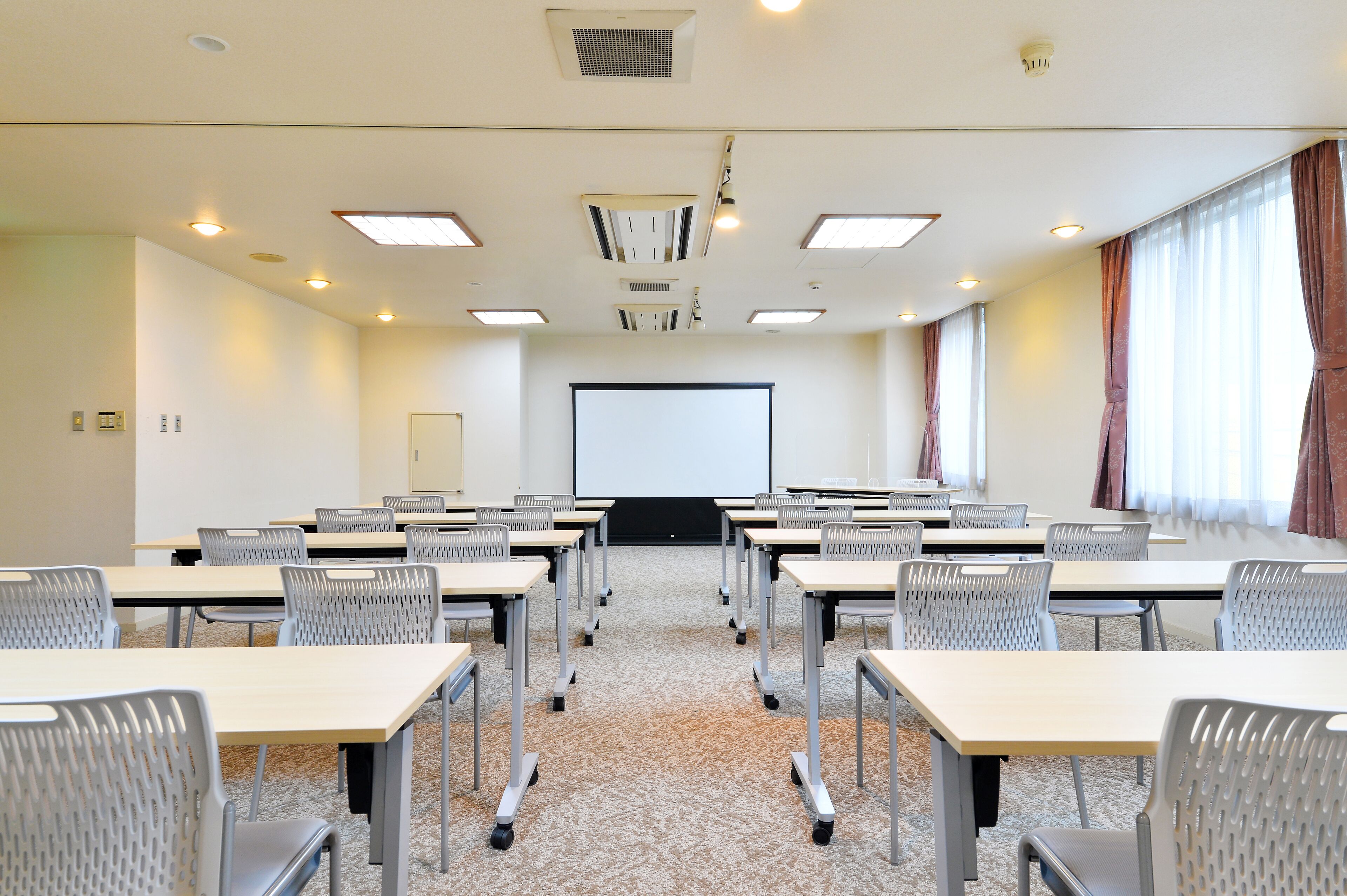 A conference room with multiple tables and chairs, a projector screen, and ceiling lights.