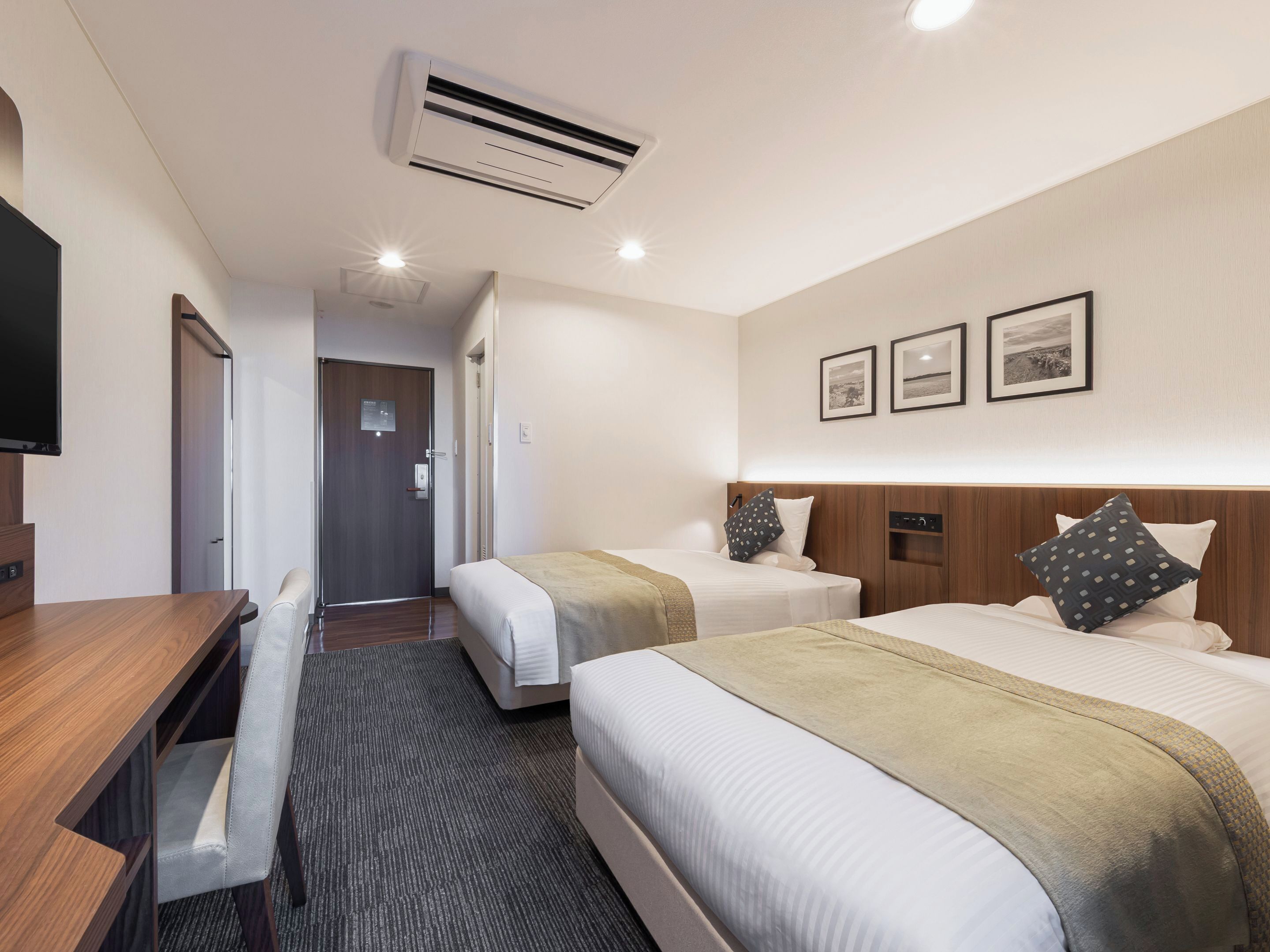Habitación de hotel con dos camas, un escritorio, una silla y un televisor.