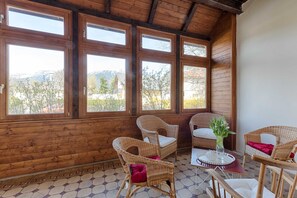 A wooden-paneled room with large windows, wicker furniture, and a tiled floor.