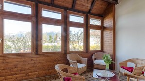 Una habitación con paneles de madera, ventanas amplias, muebles de mimbre y suelo de baldosas.