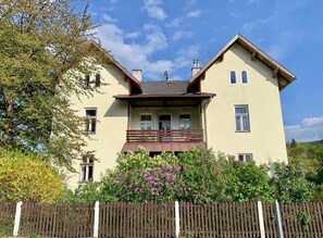 A two-story house with a balcony, a chimney, and a wooden fence. - Superior Apartment mit Einem Schlafzimmer und Gartenblick - Top 2 - Landhaus Blauer Spatz (Reichenau an der Rax)