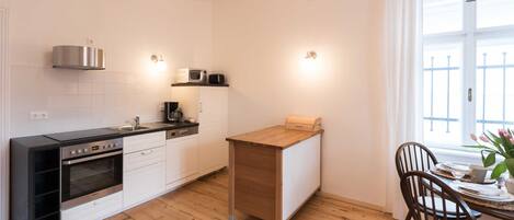 A modern kitchen with white cabinets, a wooden dining table, and a window with white curtains.