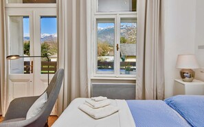 A bedroom with a bed, a chair, a lamp, and a window with a mountain view. - Studio Apartment mit Balkon und Raxblick - Top 4 - Landhaus Blauer Spatz (Reichenau an der Rax)