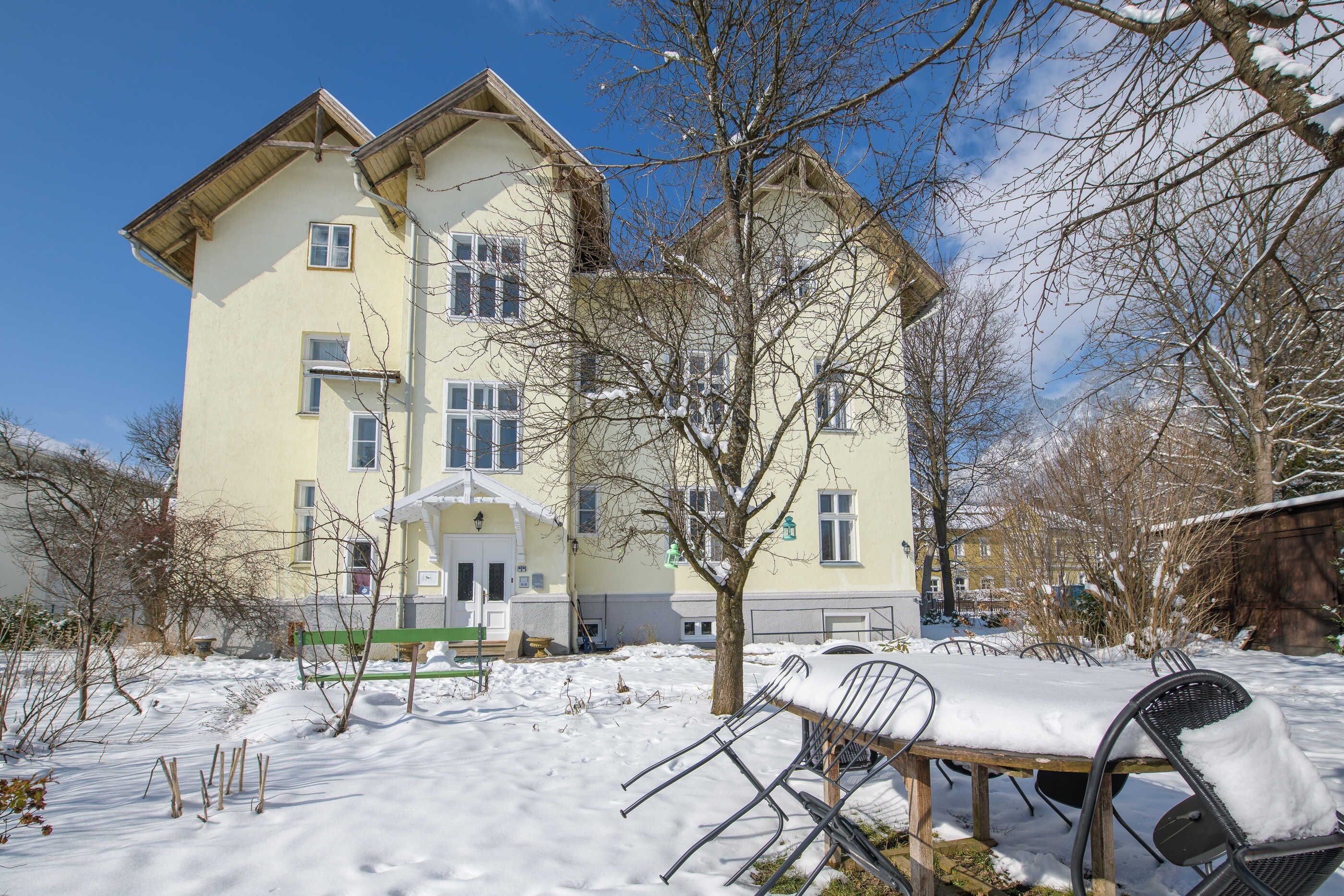 A multi-story building with a snow-covered yard, a bench, and a tree.