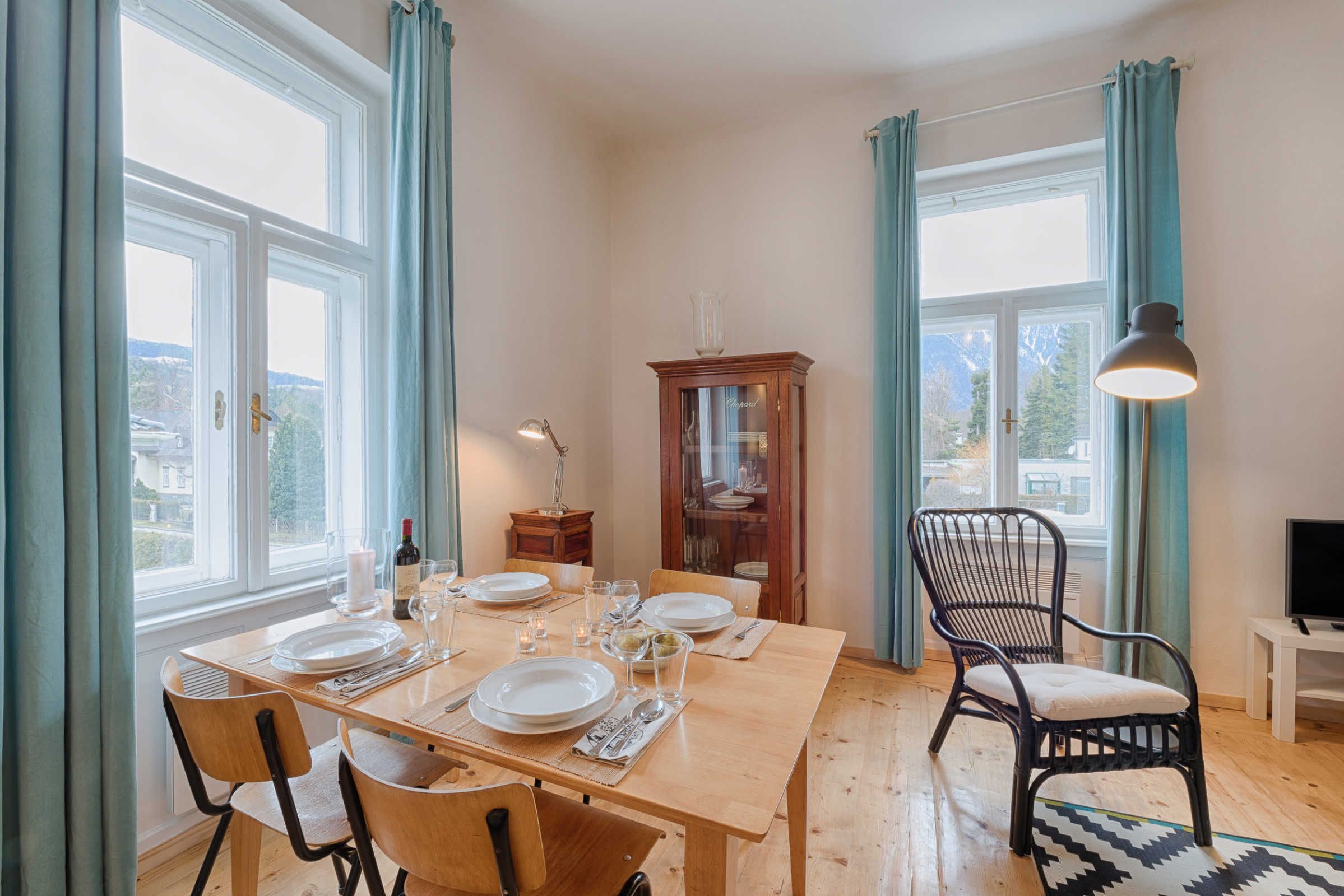 A dining area with a wooden table set for four, a cabinet, a chair, and a television on a stand.