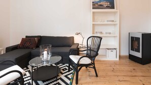 Un salon moderne comprenant un canapé, une table ronde en verre, un fauteuil noir, une bibliothèque blanche et un téléviseur.