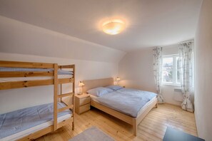 Une chambre avec des lits superposés, un lit simple, des lampes de chevet, une fenêtre avec des rideaux et un luminaire au plafond.