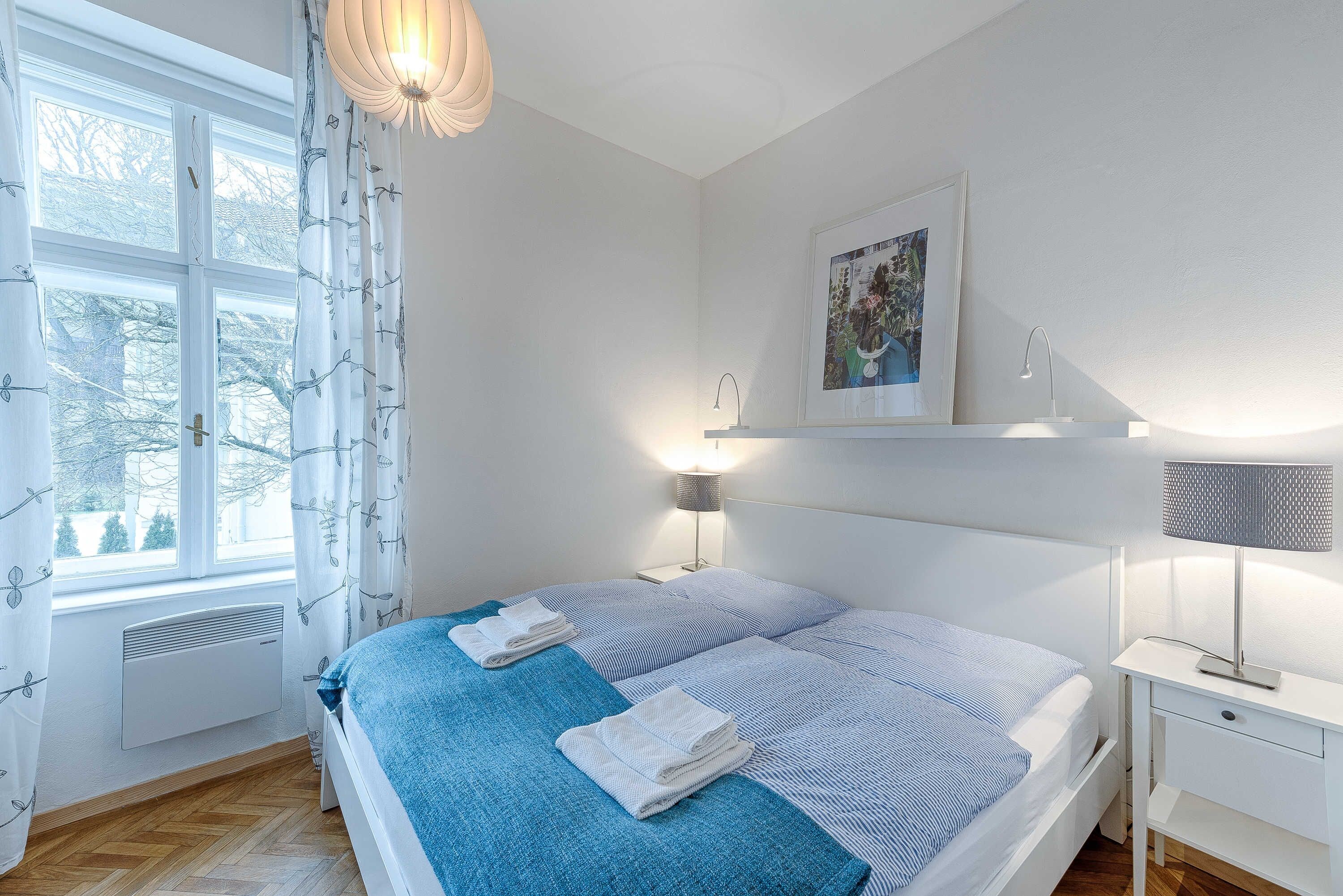 A bedroom with a bed, bedside table, lamp, and a window with curtains.