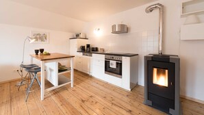 Een moderne keuken met witte kasten, een houten eettafel, een inbouwoven, een fornuis en een hanglamp.