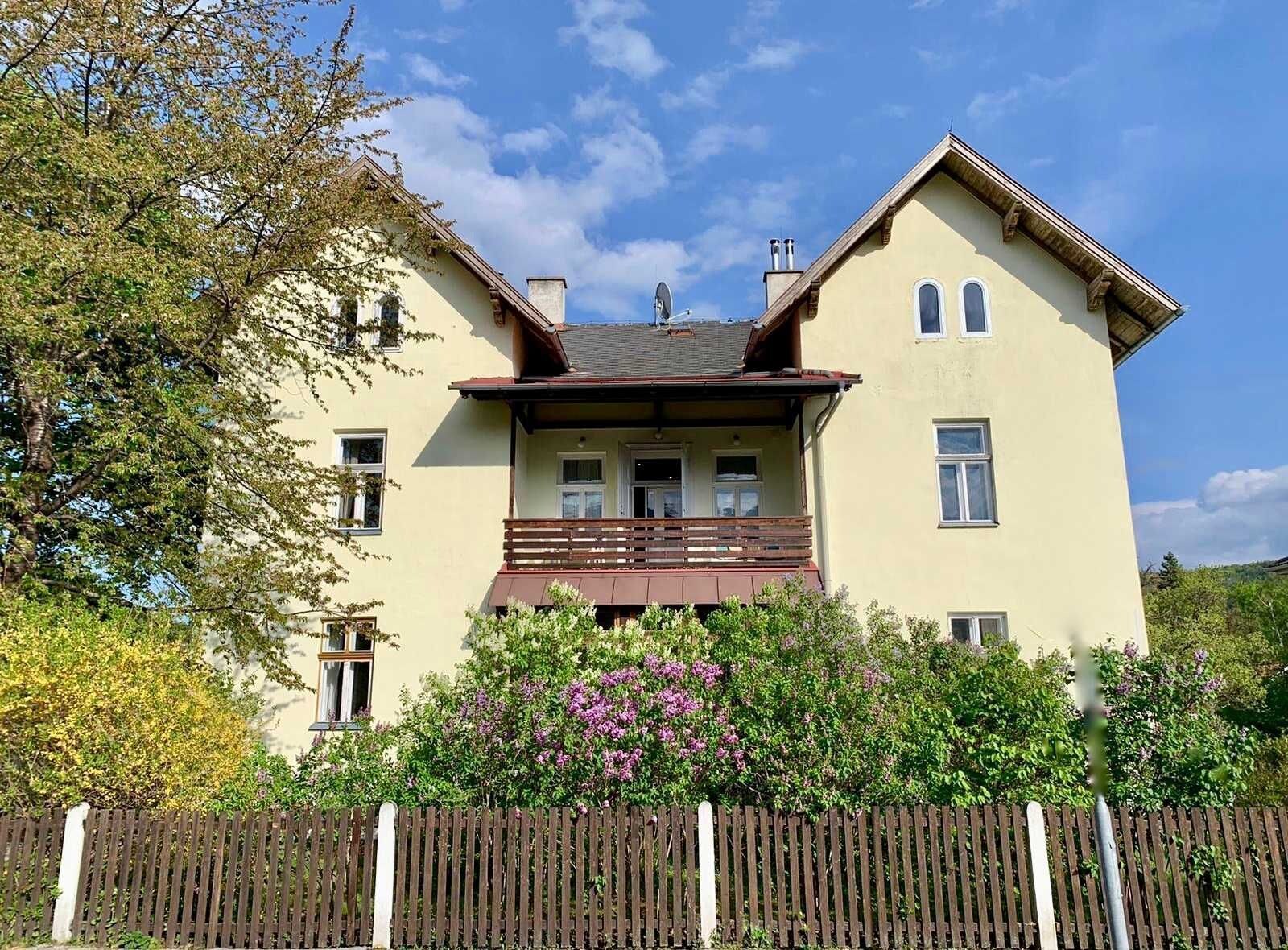 A two-story house with a balcony, a chimney, and a wooden fence.
