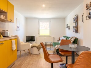 Un espace de vie compact comprenant un coin cuisine, un coin repas et un espace détente avec un téléviseur et une fenêtre.