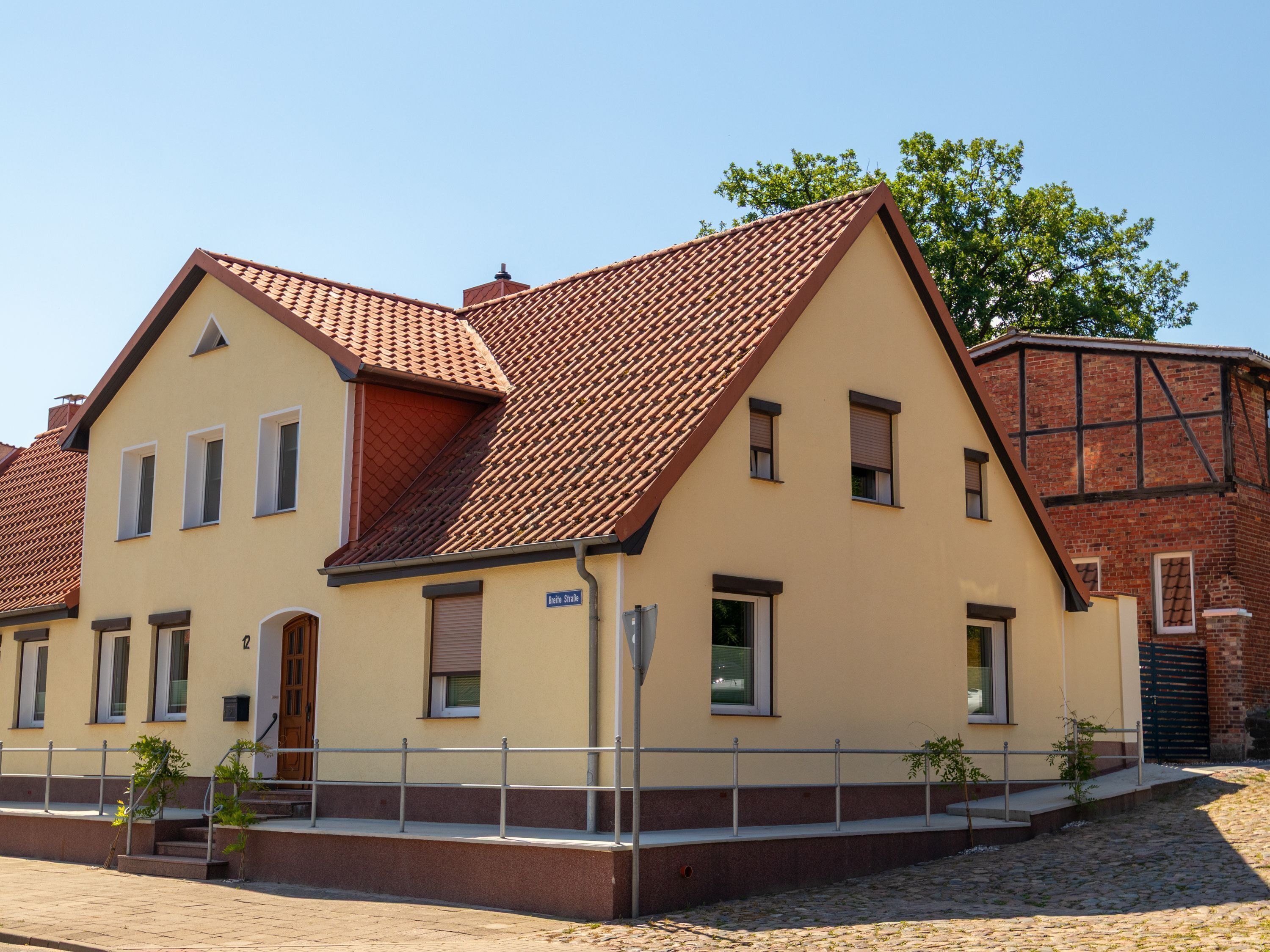 A two-story building with a red-tiled roof, a beige facade, and a small front garden.