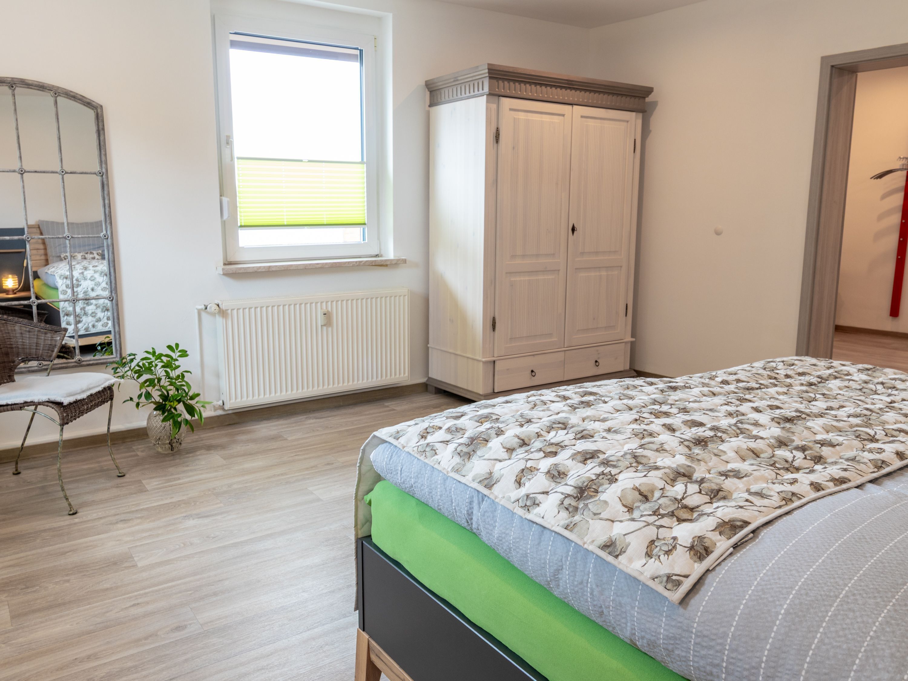 Une chambre à coucher avec un lit, une commode, une chaise, une fenêtre et un radiateur.