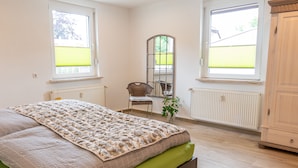 A bedroom with a bed, a chair, a mirror, and a radiator. - Duggis Feriendomizil - Ferienwohnung (Wolgast)