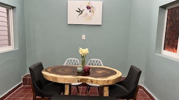 A dining area with a round wooden table, black chairs, and a bench. There is a painting on the wall above the table.