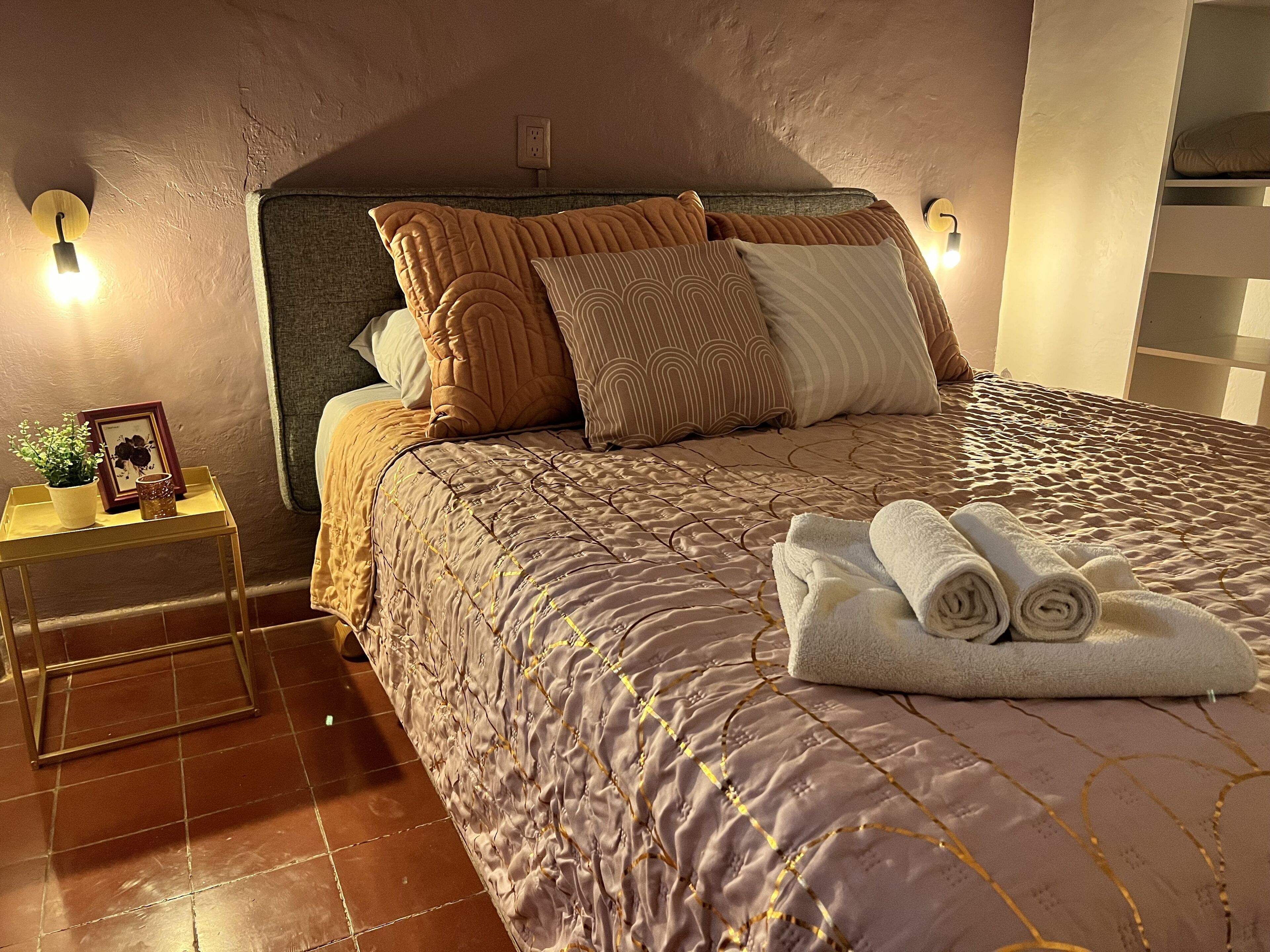 A neatly made bed with a patterned bedspread, multiple pillows, and a rolled towel on the side.