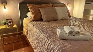 Un lit bien fait, avec une couvre-lit à motifs, plusieurs oreillers et une serviette enroulée posée sur le côté.
