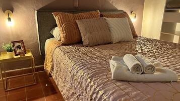 A neatly made bed with a patterned bedspread, multiple pillows, and a rolled towel on the side.