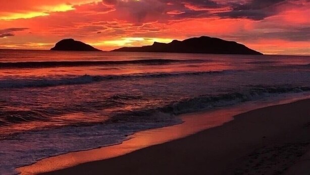 Une plage avec un coucher de soleil et des montagnes en arrière-plan.